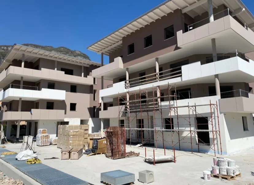 New apartment building under construction with scaffolding, building materials, and paint cans on a sunny day.
