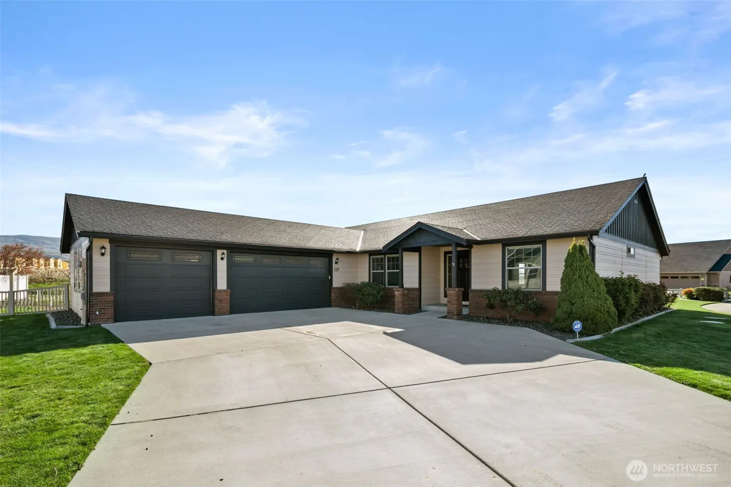 Beige single-story home with a gray roof, a two-car garage, and a concrete driveway under a blue sky.