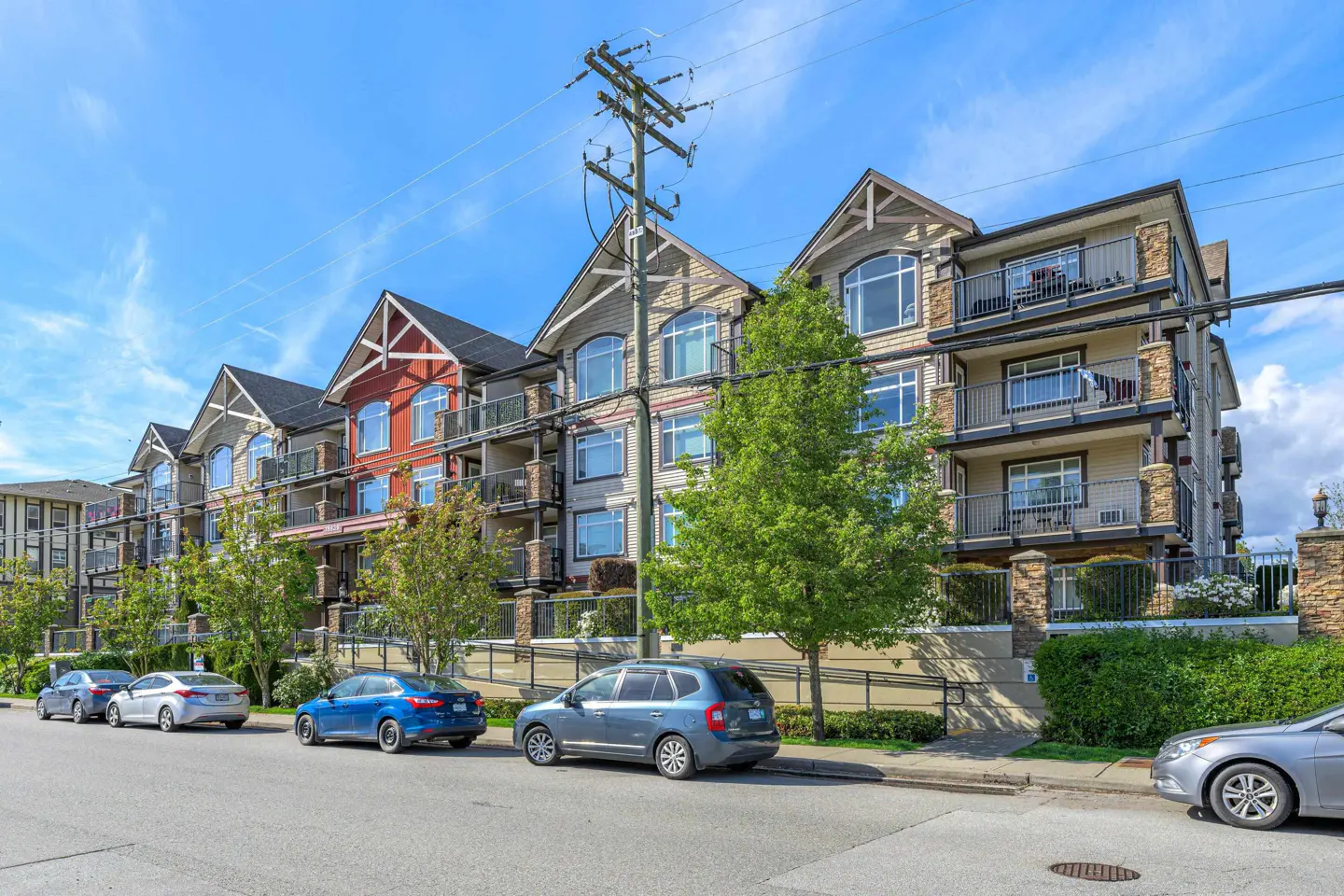 Exterior view of a multi-story apartment building with balconies and parked cars on the street.