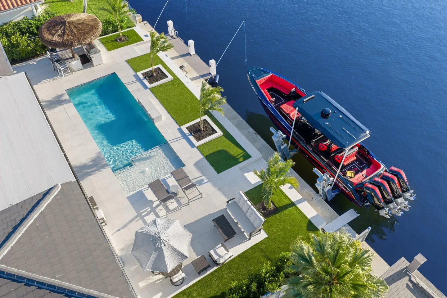 Aerial view of a luxury waterfront home with a pool, patio, and a large red and blue boat docked on the canal.