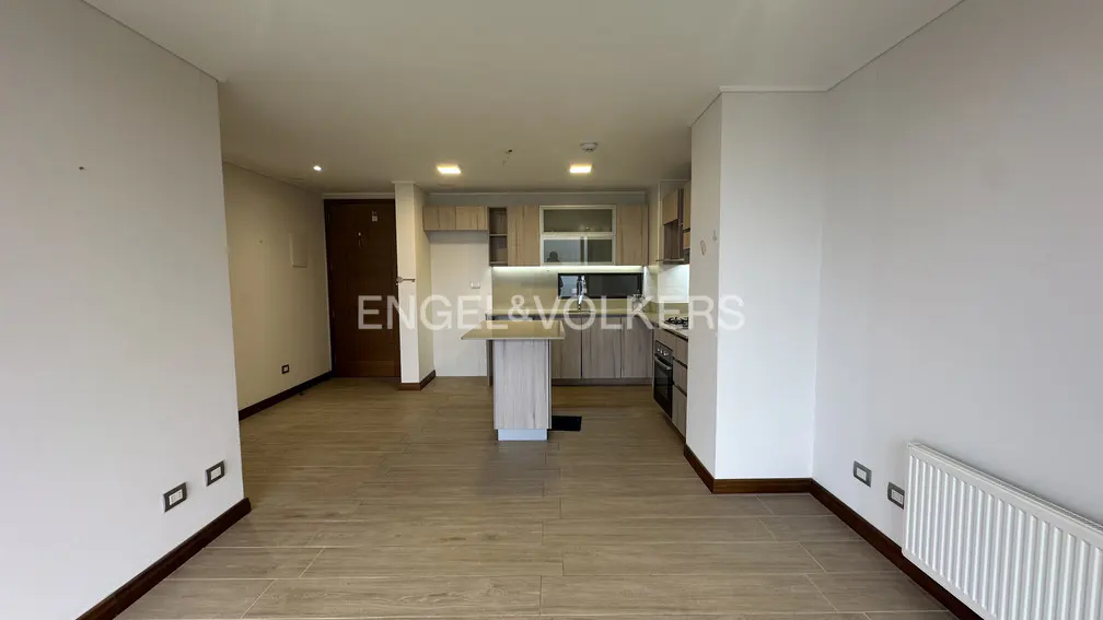 A bright, modern apartment interior with light wood floors, white walls, and a compact kitchen area.