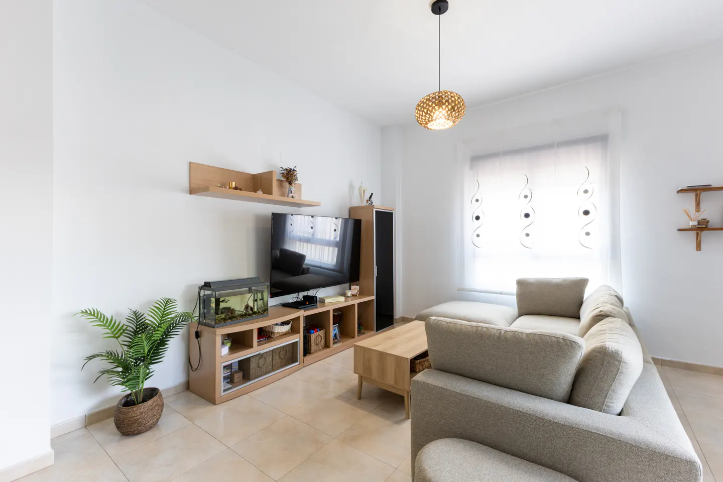 Bright living room with a beige sectional sofa, wood TV stand with aquarium, and a woven pendant light.