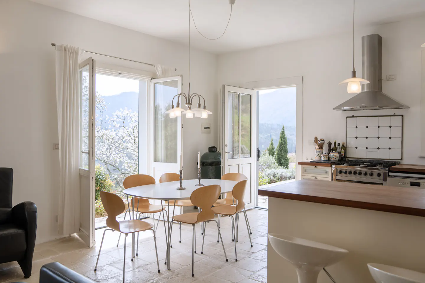 Bright, airy kitchen with white walls, a round table with six chairs, and open doors to a scenic view.