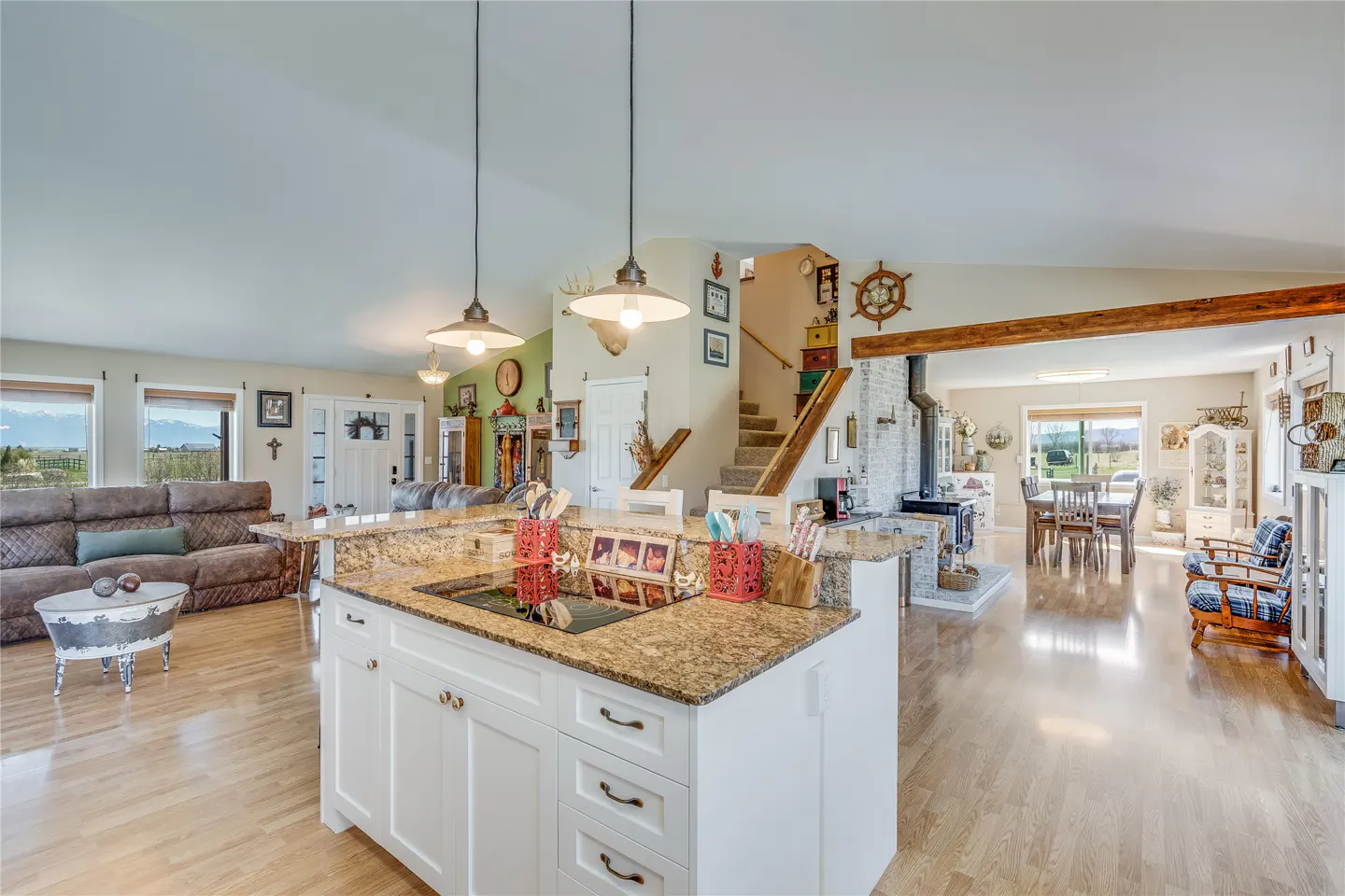 Open-concept home interior with a white kitchen island, granite countertops, and light wood floors. Living and dining areas visible.