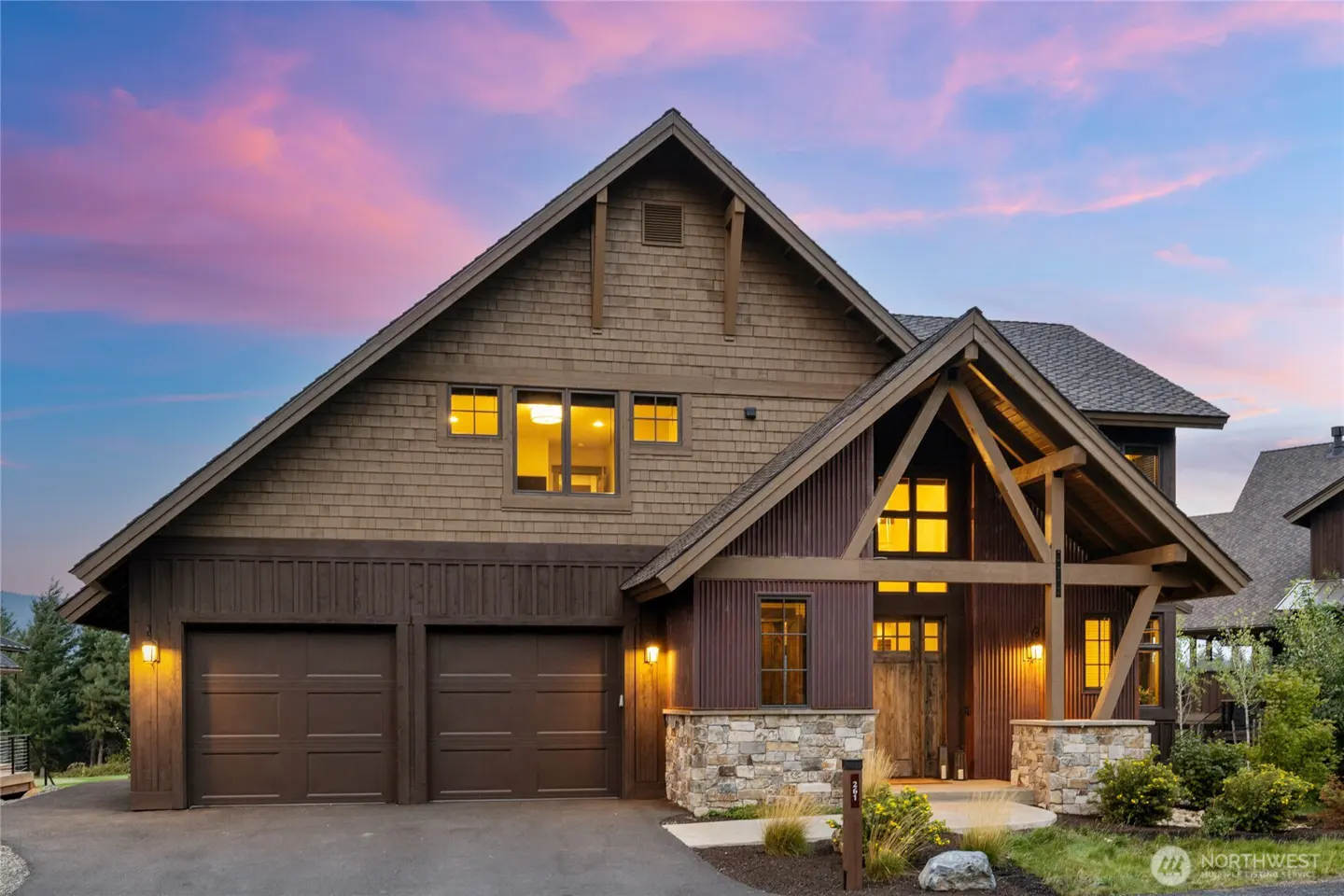 Exterior view of a two-story brown house with a two-car garage and stone accents at dusk.