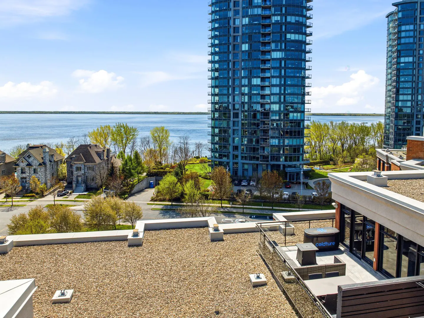 Rooftop view of a city with blue glass high-rise buildings, a lake, and houses. A patio set is visible on the roof.