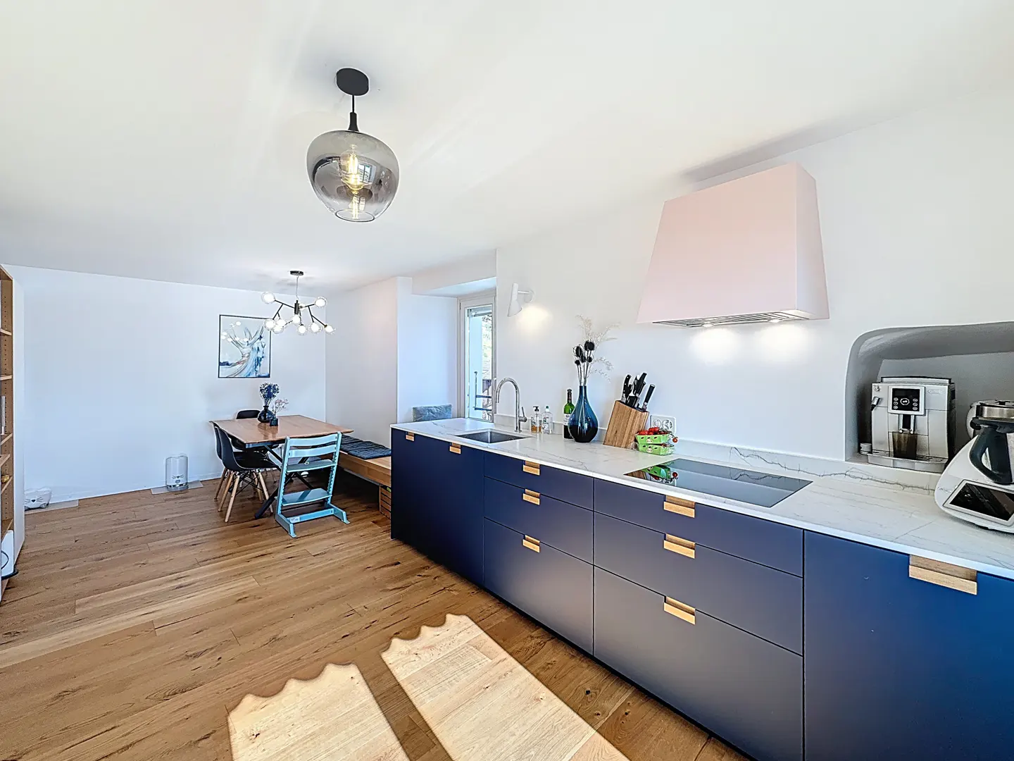 Modern kitchen with navy blue cabinets, white countertops, a pink range hood, and a dining area with wood floors.