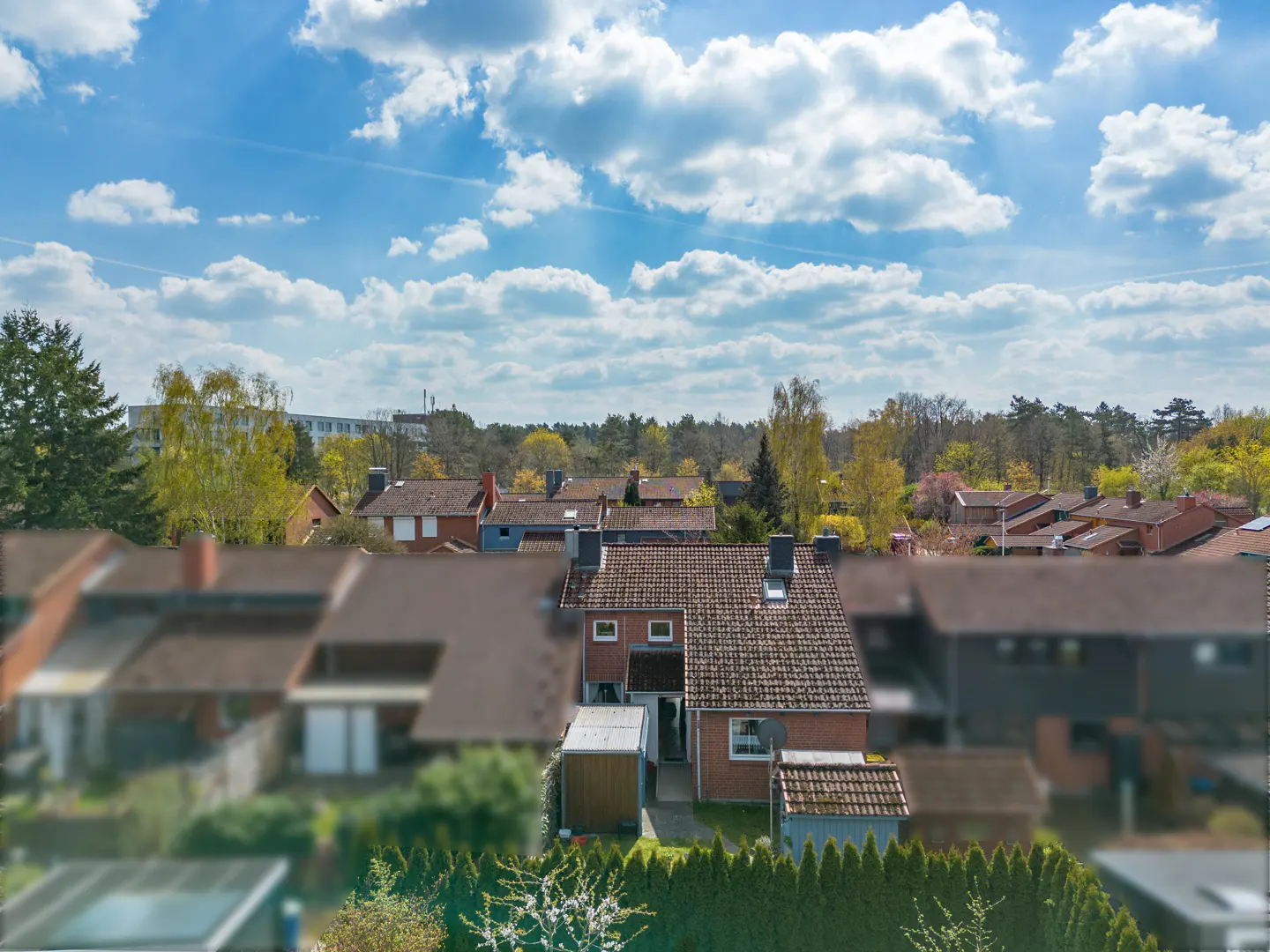 Aerial view of a residential neighborhood with red-roofed houses under a blue sky with fluffy white clouds.