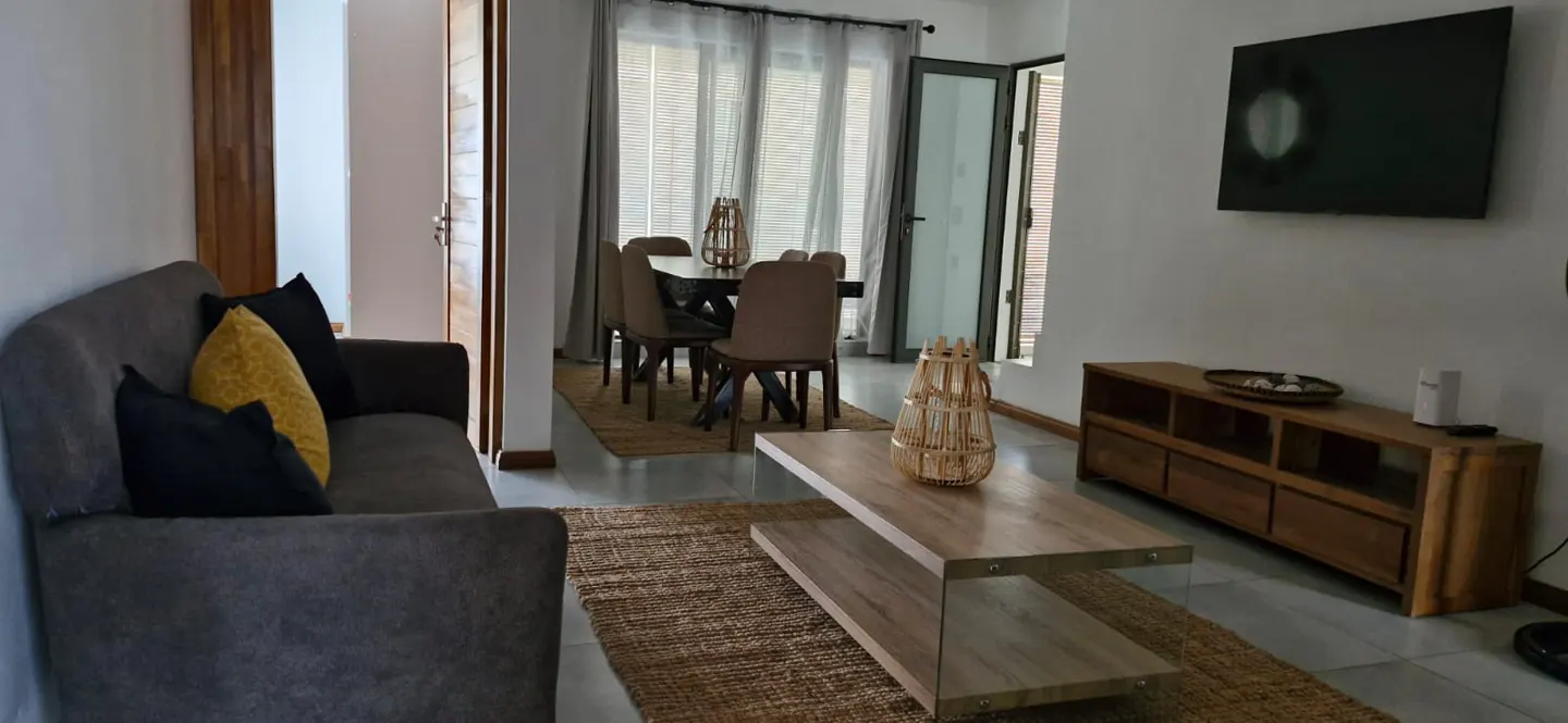 Living room with a gray sofa, yellow and black pillows, a wooden coffee table, and a dining table with chairs in the background.
