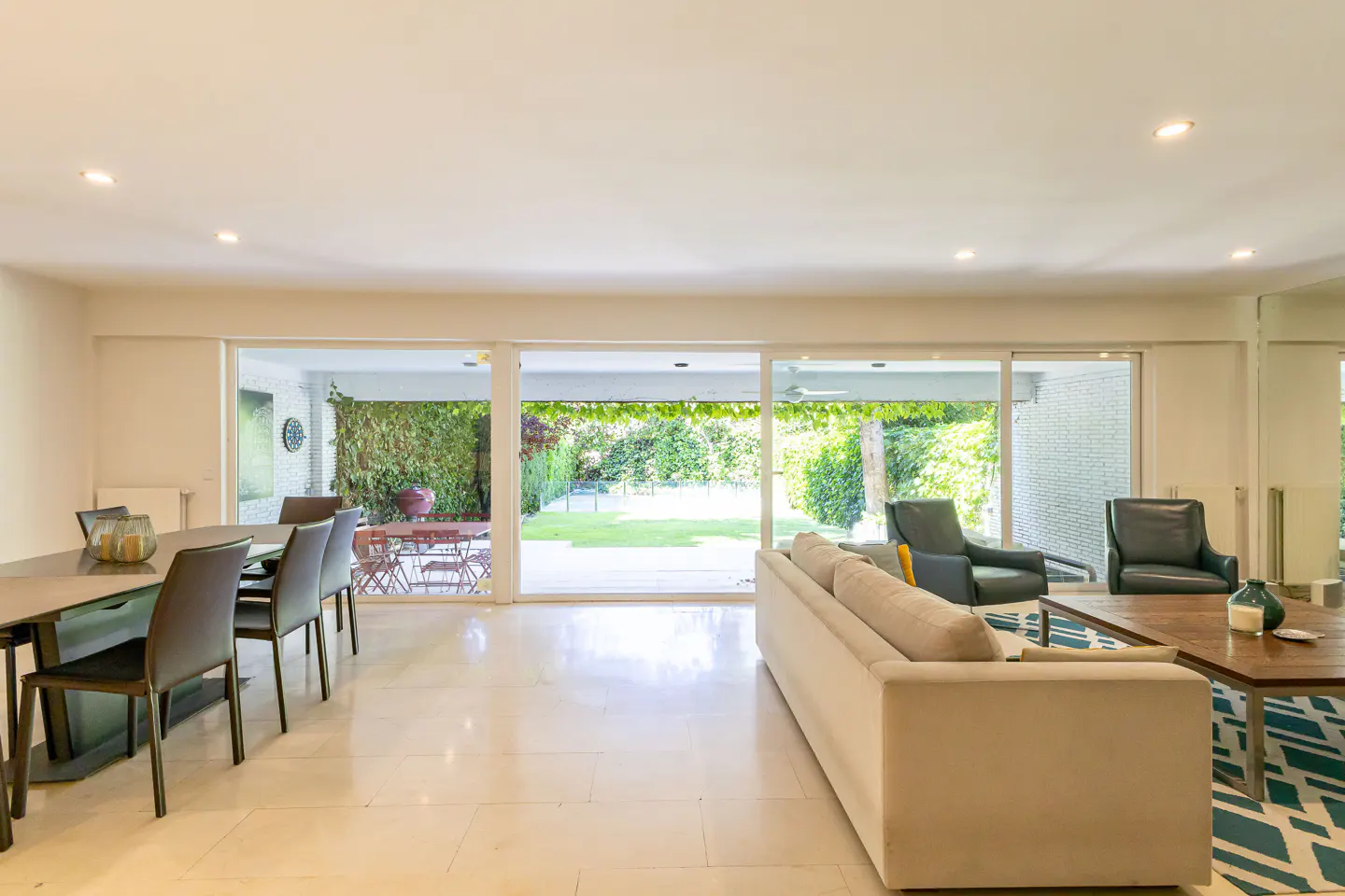 Bright, open living space with dining table, sofa, and chairs. Large sliding doors lead to a green backyard.