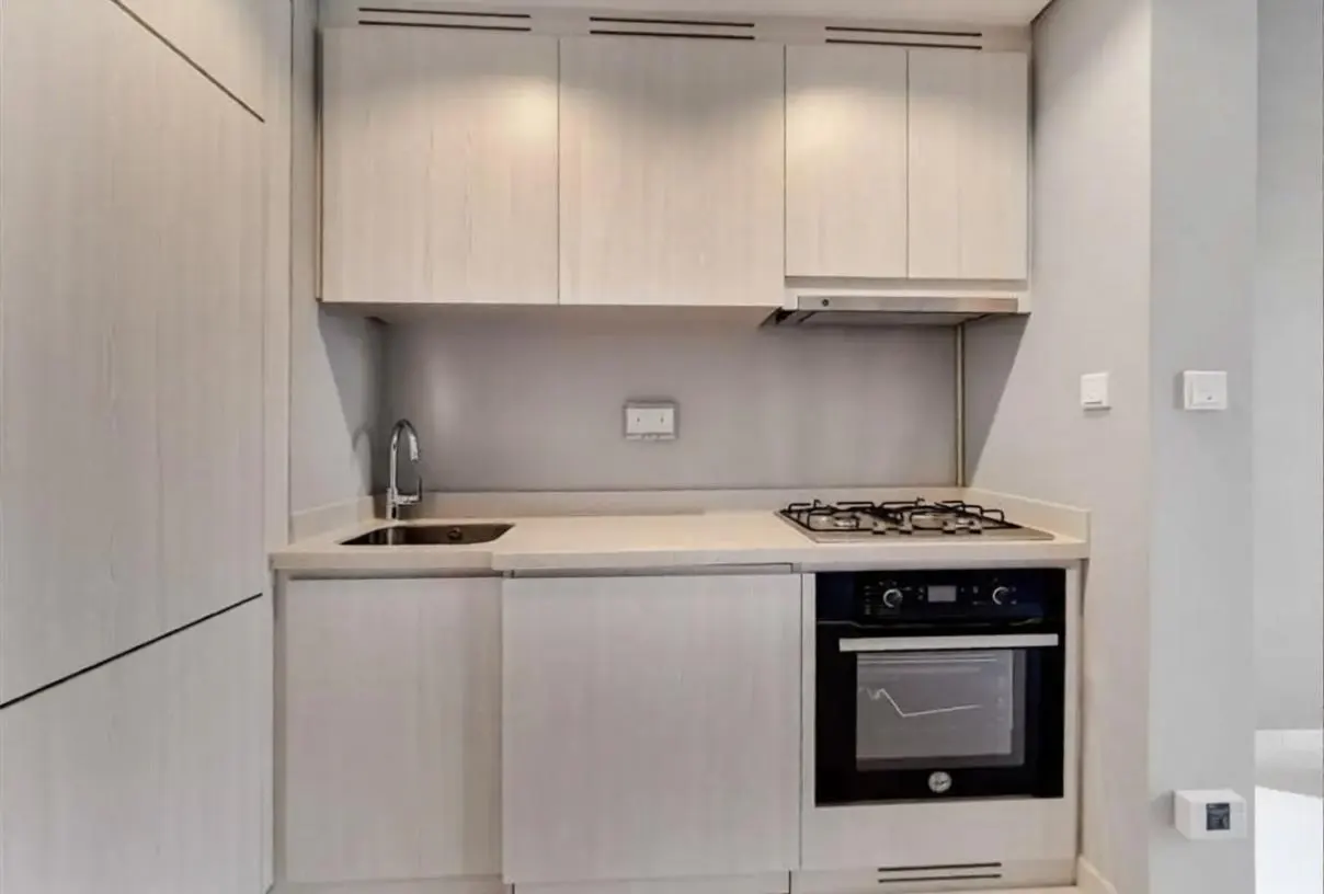 A compact kitchen with light wood cabinets, a stainless steel sink, a gas stovetop, and a built-in oven.