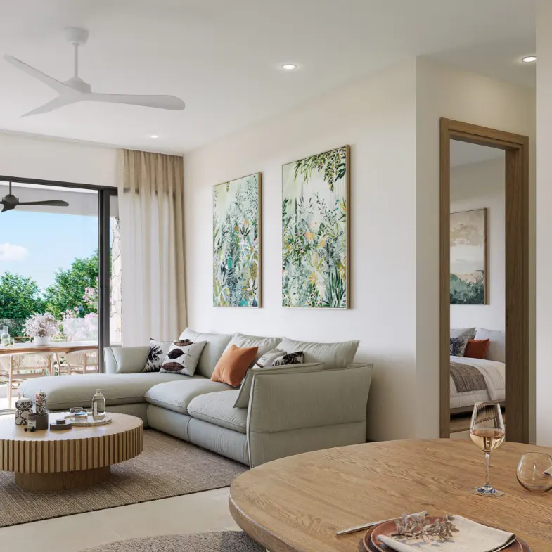 Bright living room with a gray sectional sofa, round wood coffee table, and two botanical art prints. A bedroom is visible through a doorway.