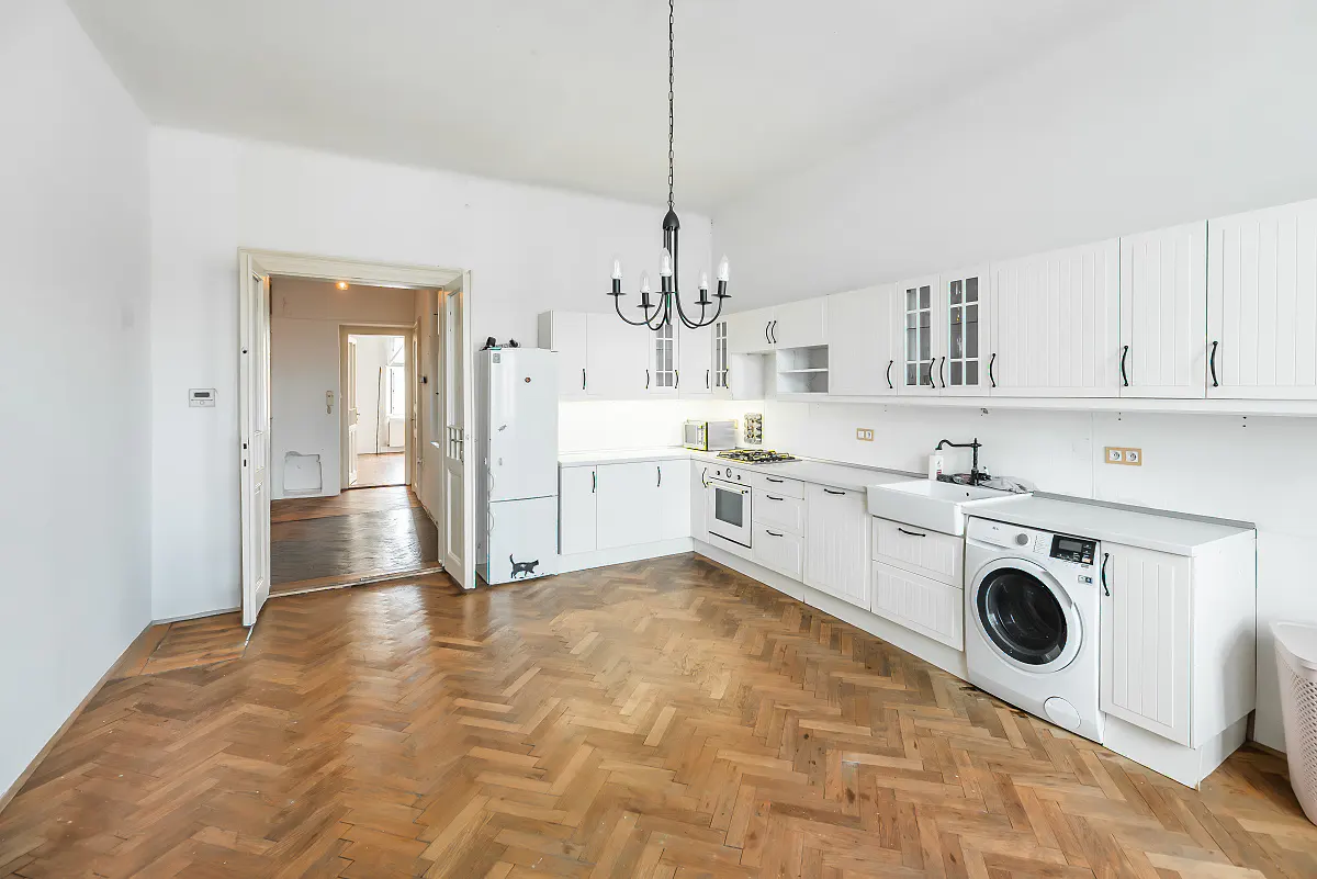 Bright kitchen with white cabinets, herringbone wood floors, a black chandelier, and a built-in washing machine.