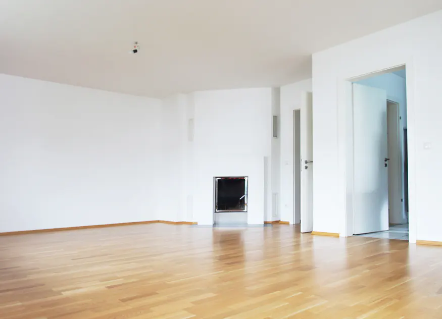 Bright, empty room with light wood floors, white walls, and a modern fireplace. Open doorways lead to other rooms.