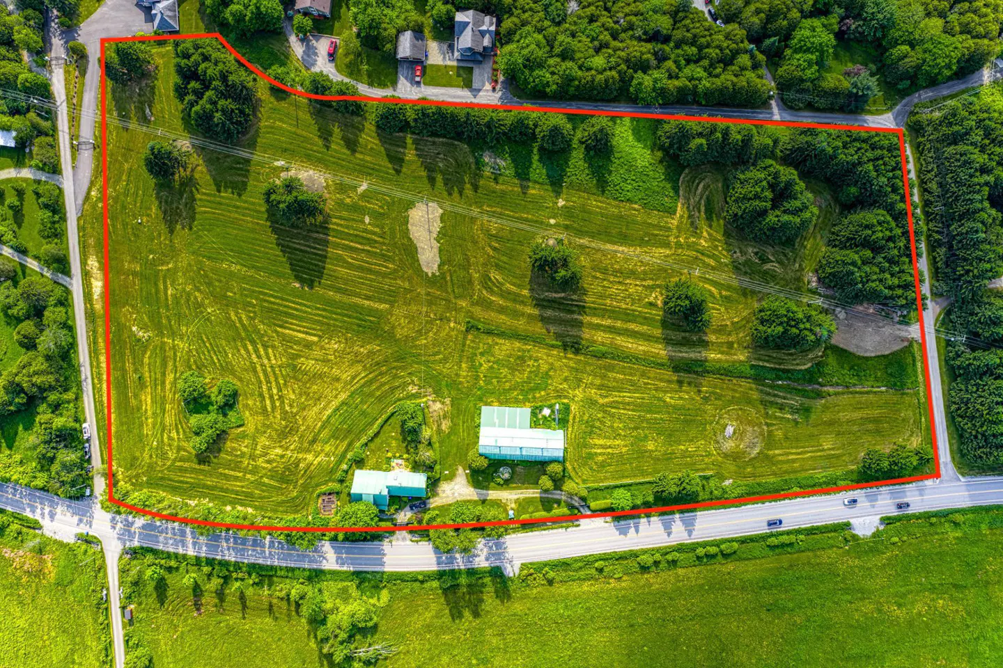 Aerial view of a large, green, grassy property outlined in red, with buildings, trees, and a road.