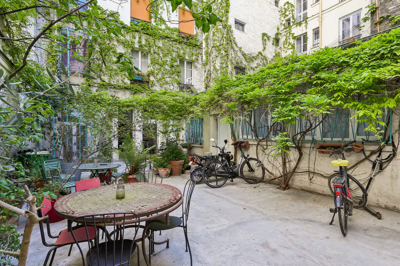 A courtyard with tables, chairs, bicycles, and buildings covered in green vines.