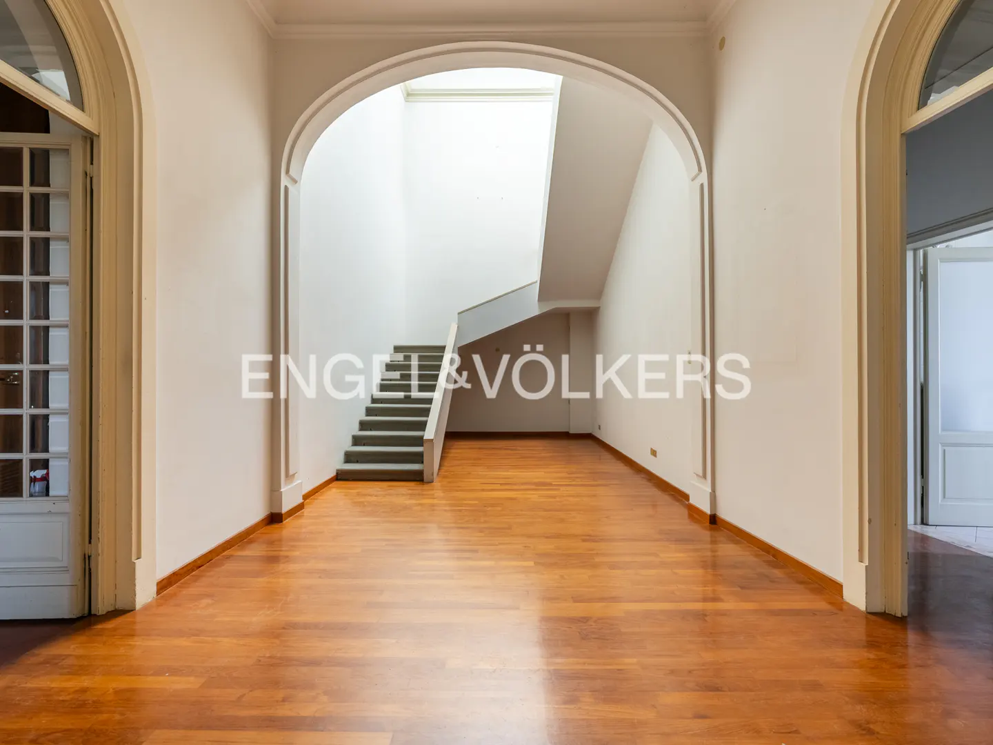 Spacious white hallway with polished wood floors, an arched entryway, and a modern staircase leading to a skylight.