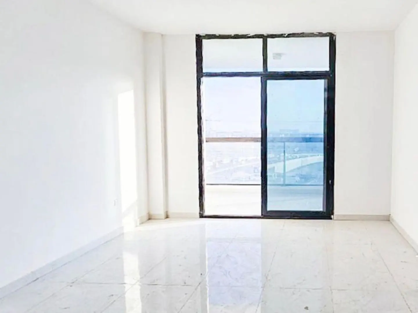 Empty room with white walls and marble floor. A black-framed window shows a city view.