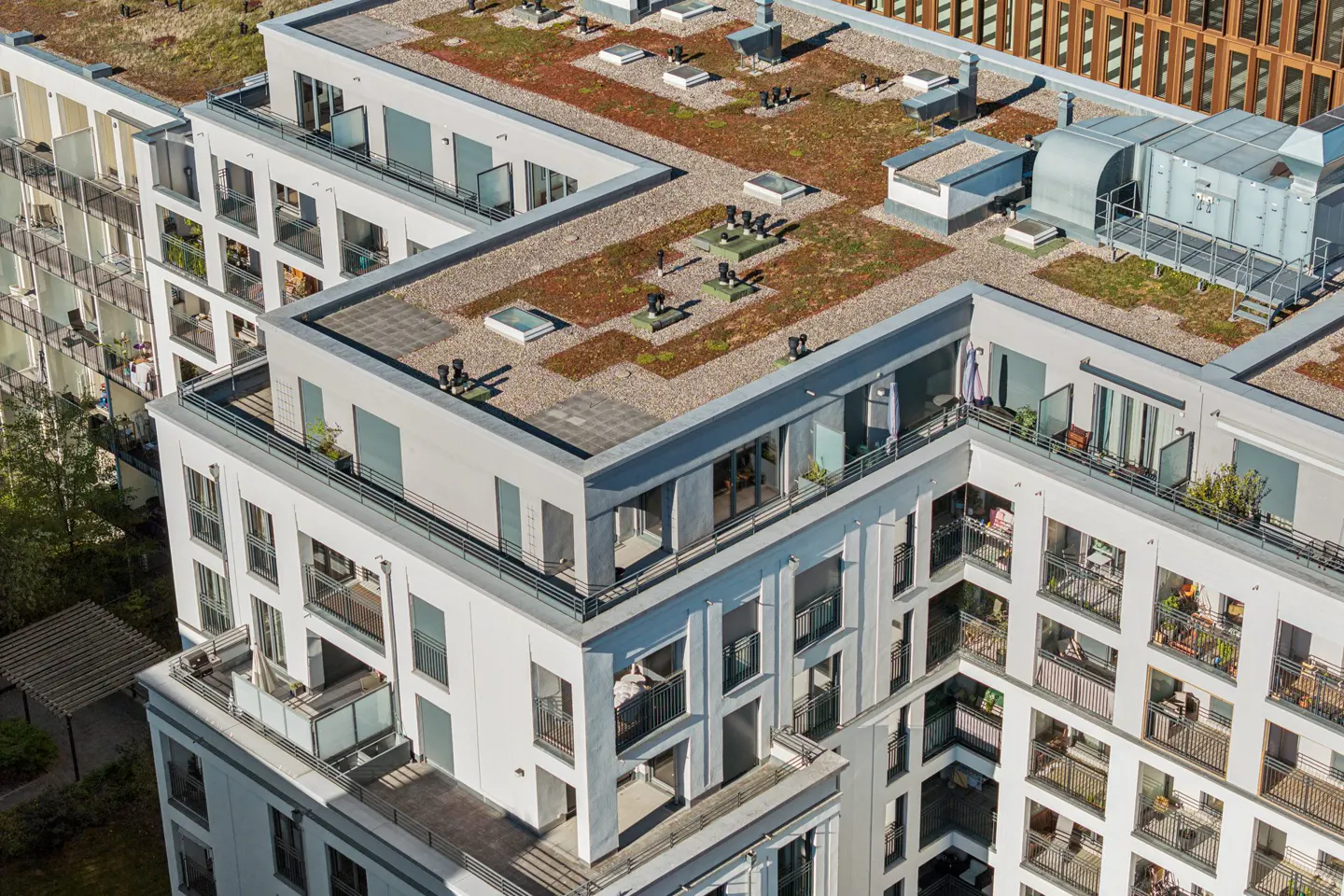 Aerial view of a modern white apartment building with balconies and a green roof.