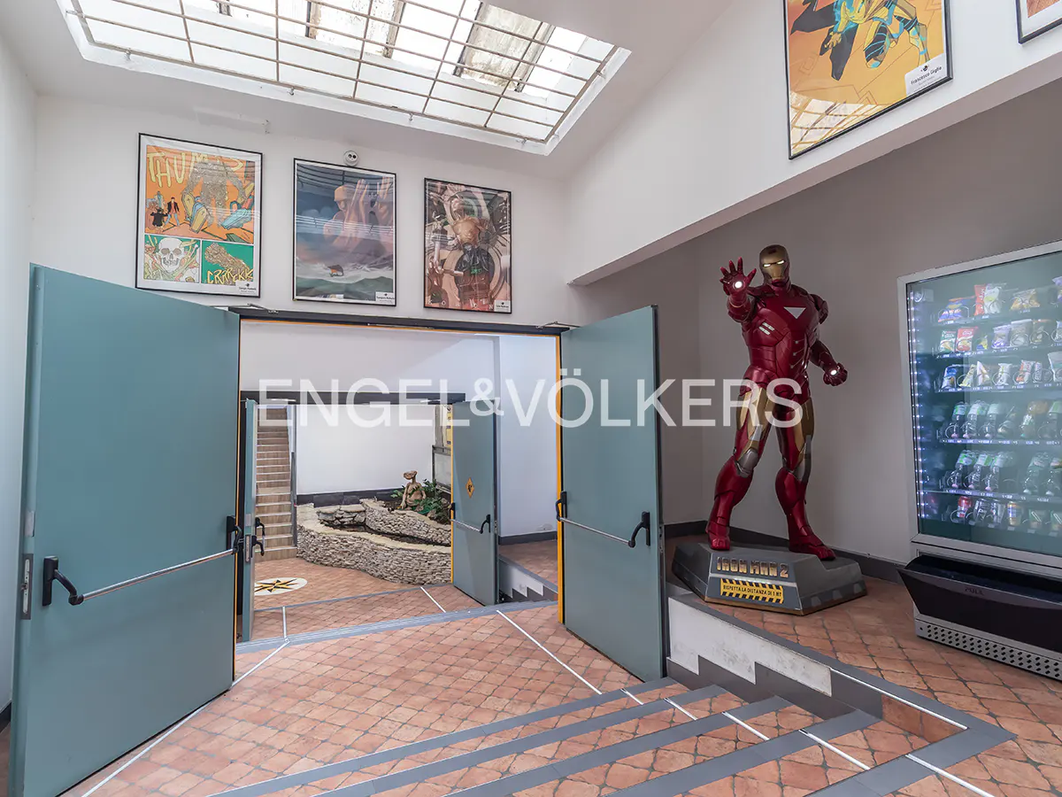 Interior view of a building with an Iron Man statue, vending machine, and artwork. The floor is tiled in red and gray.