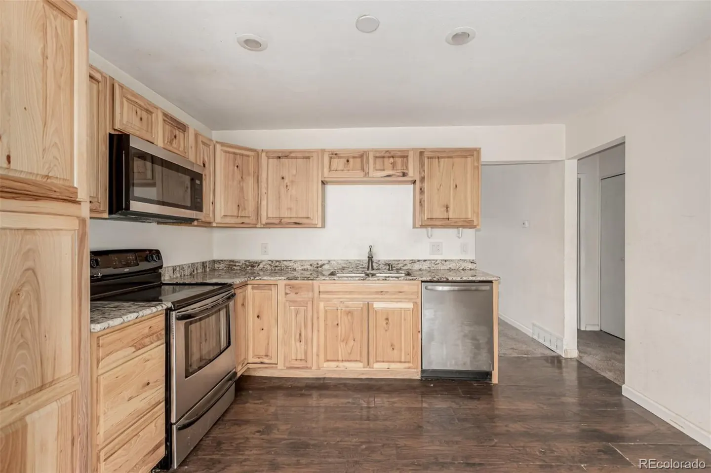 A kitchen with light wood cabinets, stainless steel appliances, granite countertops, and dark wood floors.