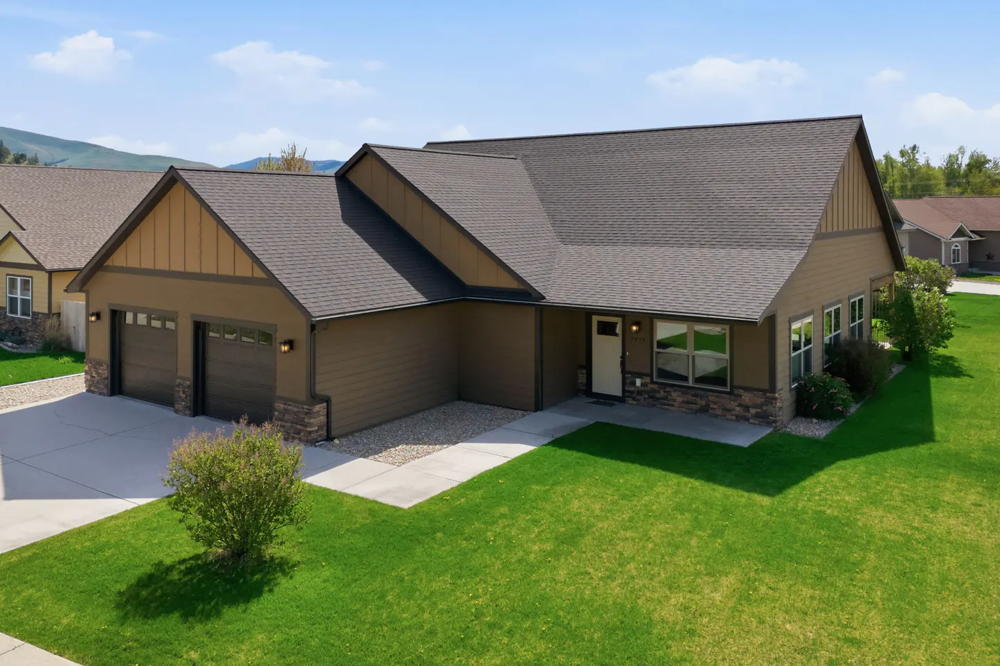 A tan single-story house with a gray roof, a two-car garage, and a green lawn.