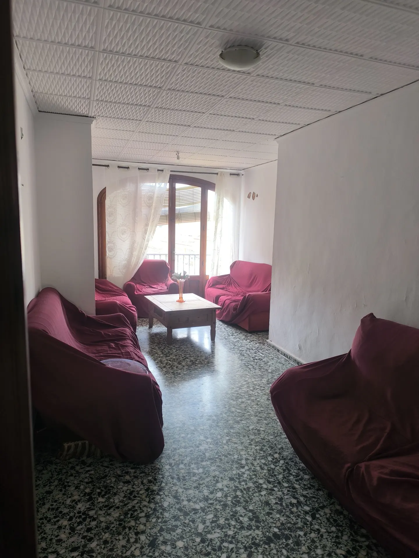 Living room with red covered sofas, a wooden coffee table, and a balcony with white curtains.