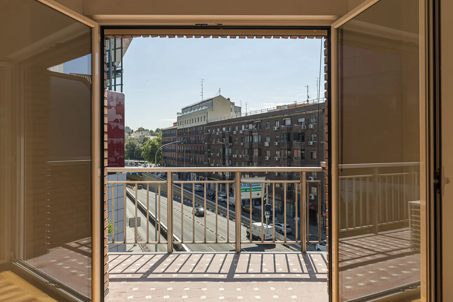 View from an open balcony with metal railings overlooking a busy city street with buildings and traffic.