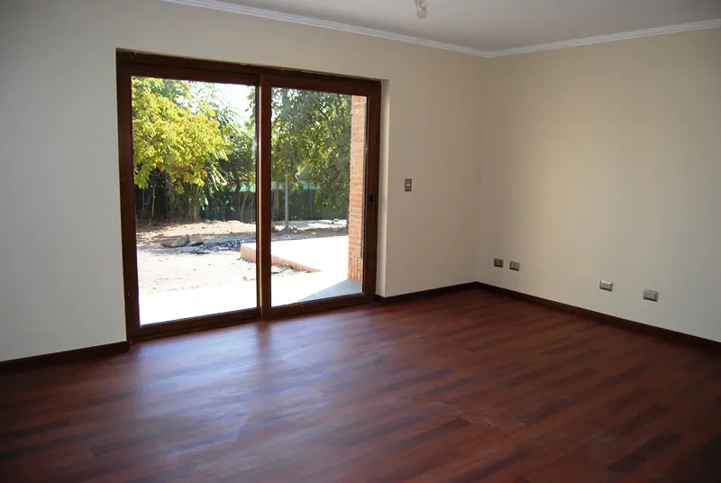 Empty room with dark wood floors, cream walls, and a sliding glass door to a yard with trees.