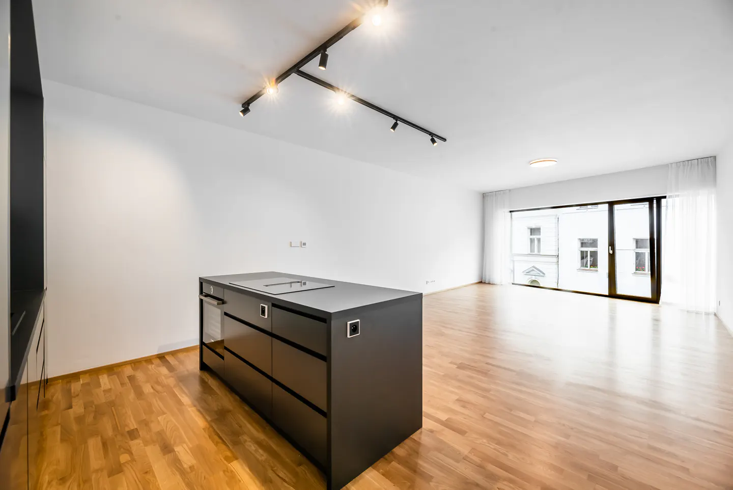 Bright, modern apartment with wood floors, white walls, and a black kitchen island. A large window shows a building across the street.
