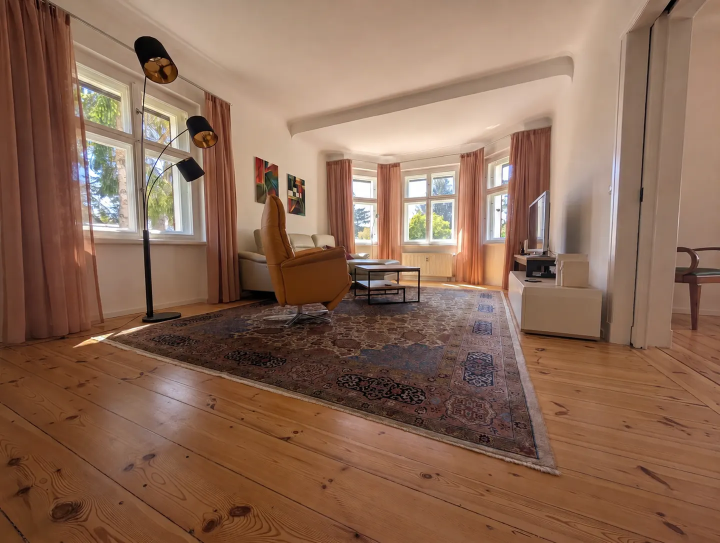 Bright living room with wood floors, a large patterned rug, a tan recliner, and a modern floor lamp by the window.