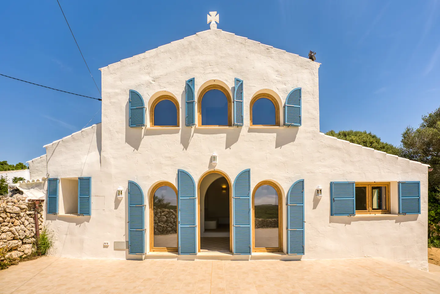 Exterior of a white stucco house with blue shutters and arched windows under a clear blue sky.