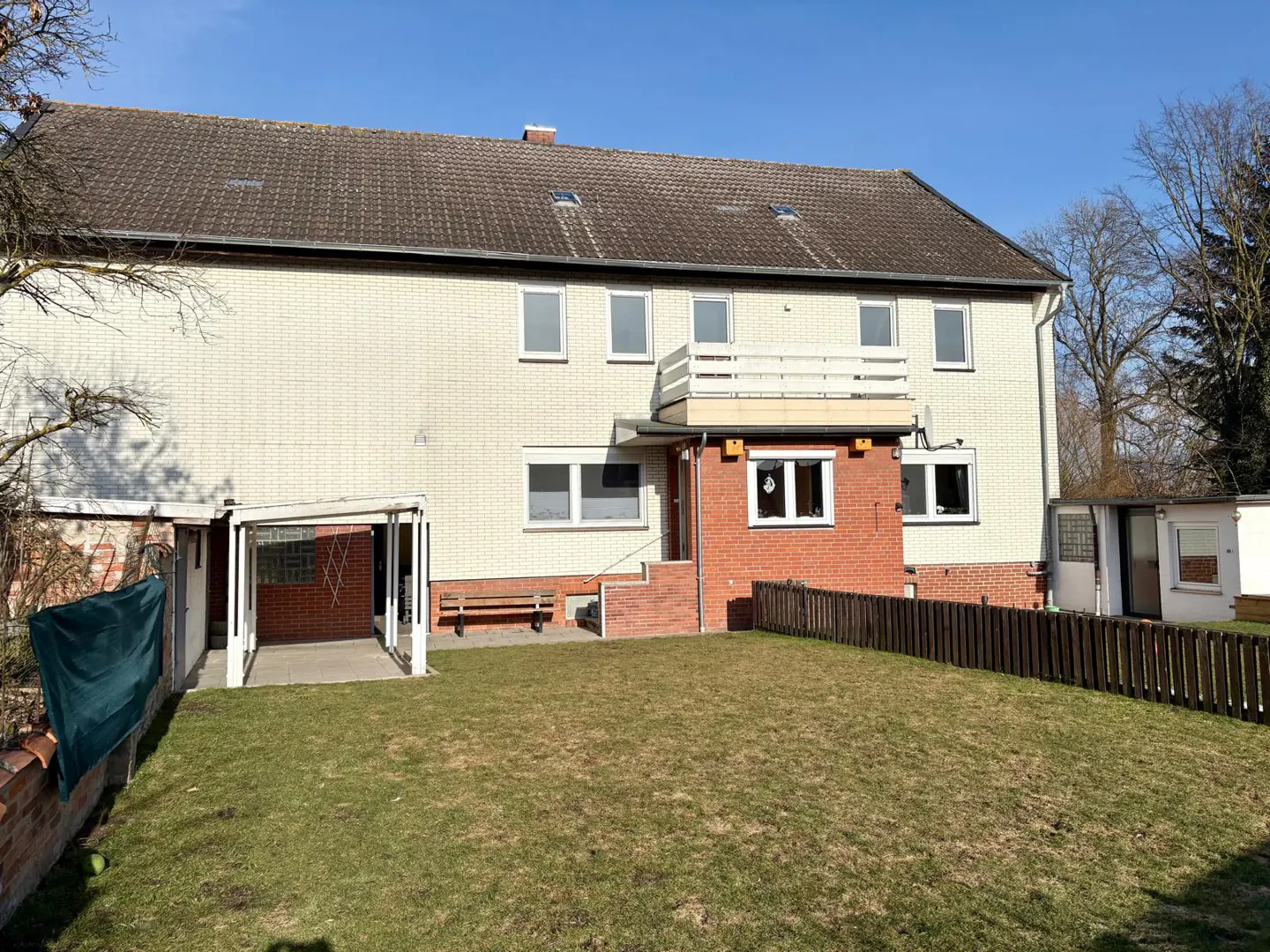 Exterior view of a two-story house with a brick facade, a balcony, a carport, and a green lawn.