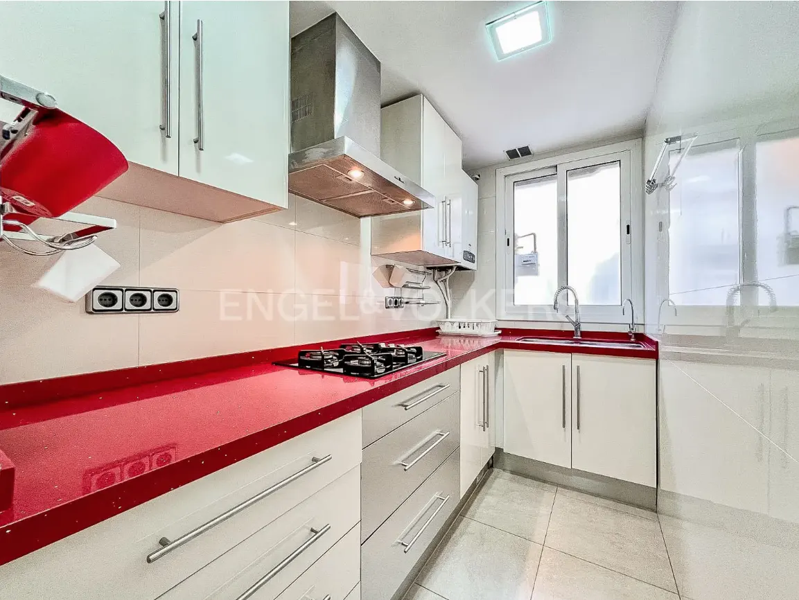 Bright kitchen with white cabinets, red countertops, stainless steel appliances, and a window.