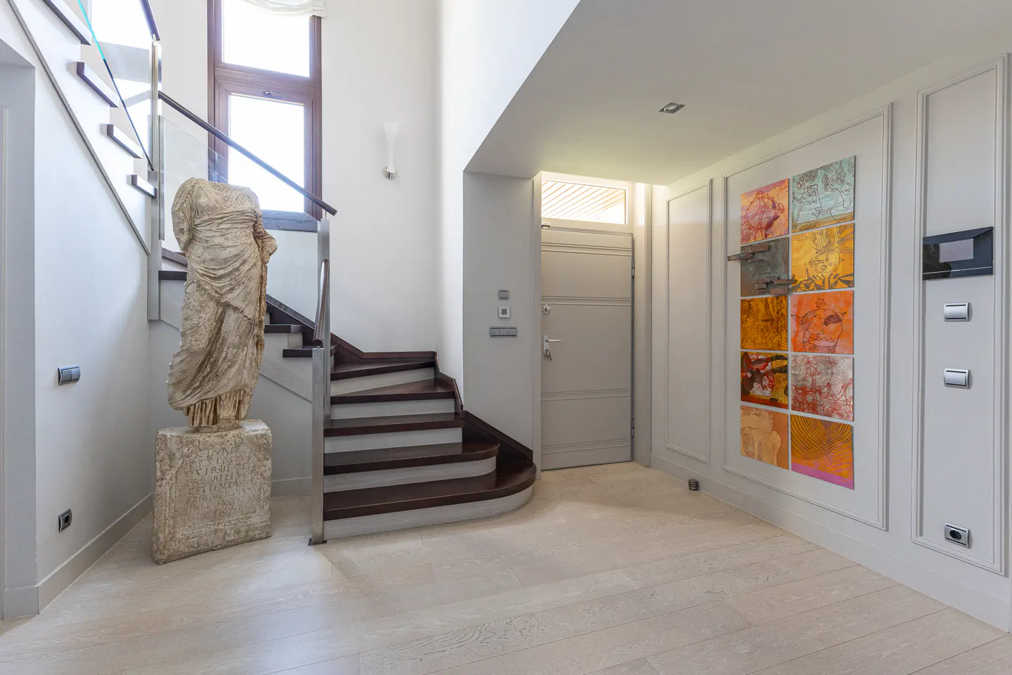 Modern entryway with a stone statue, wooden staircase, and a wall display of colorful square art panels.