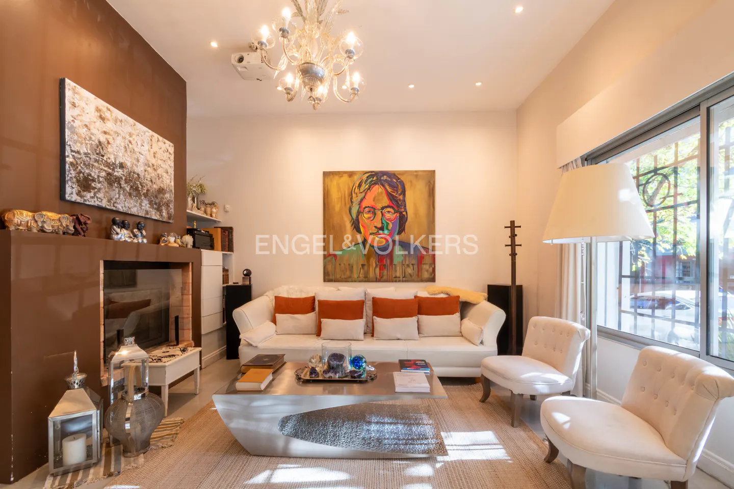 Living room with white sofa, orange pillows, and a portrait of John Lennon above. A modern coffee table sits on a light rug.