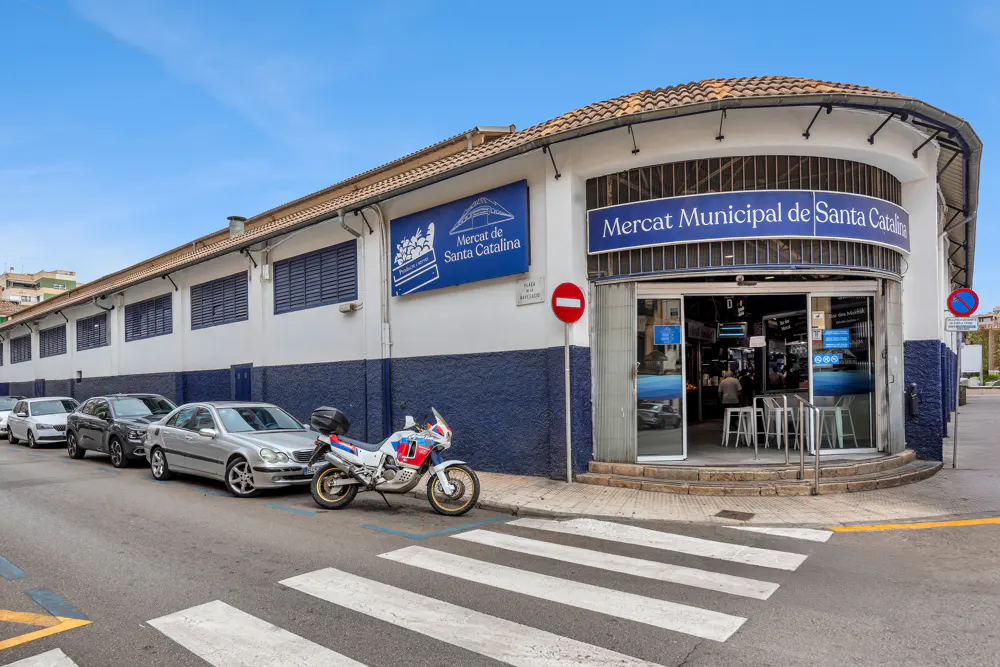 Exterior view of the Mercat Municipal de Santa Catalina, a market building with cars and a motorcycle parked outside.