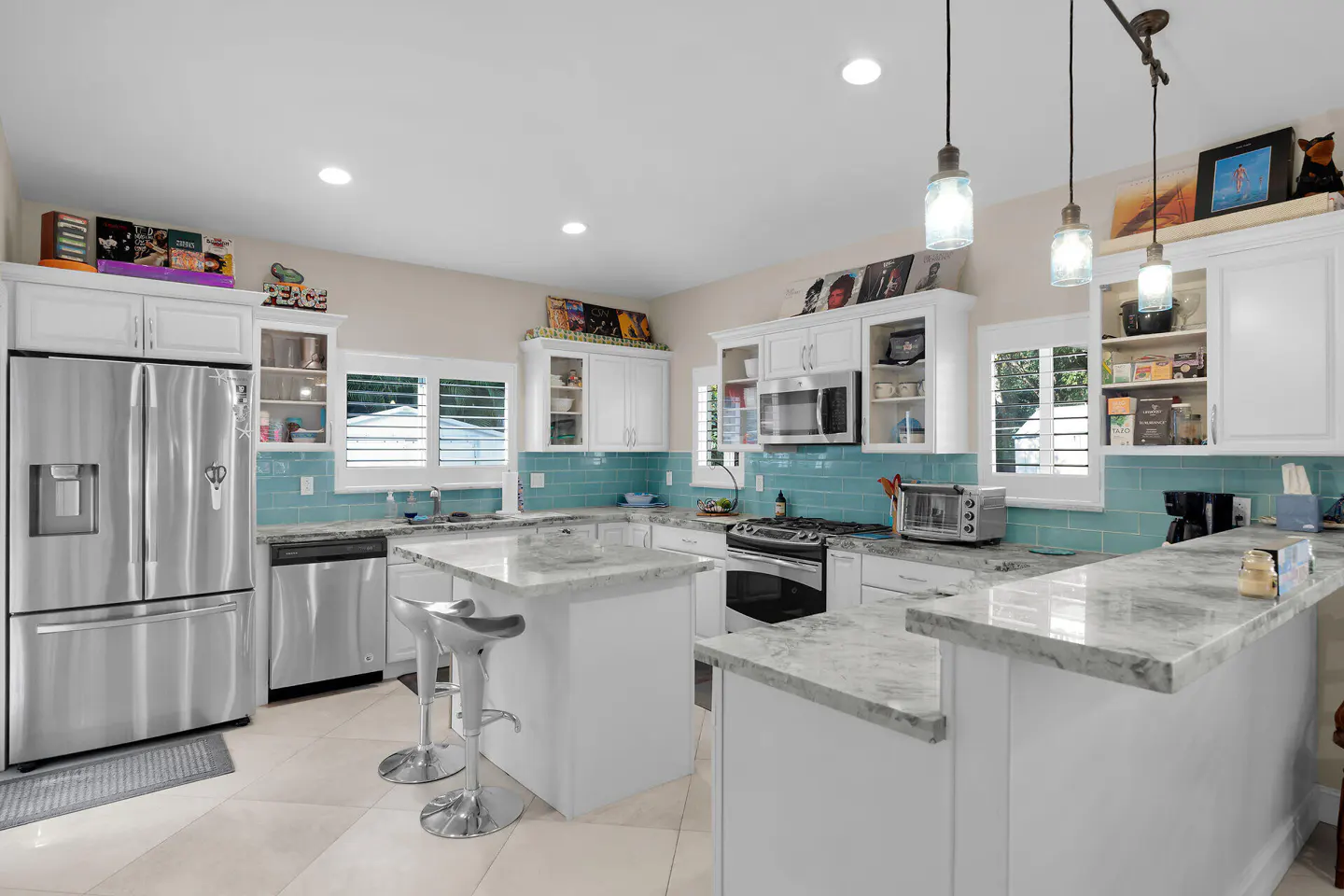 Bright kitchen with white cabinets, marble countertops, and turquoise backsplash. Stainless steel appliances and pendant lights complete the modern design.