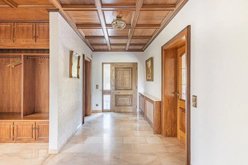 Hallway with wood paneled ceiling, marble floors, and built-in wood cabinets. A chandelier hangs from the ceiling.