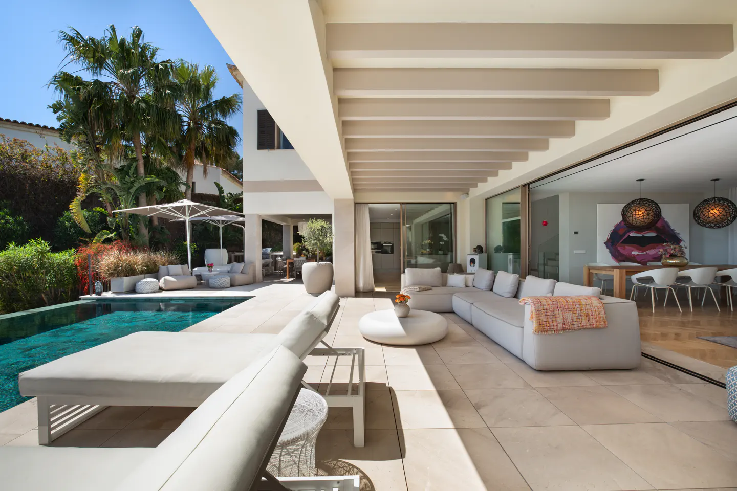 Luxury villa patio with pool, lounge chairs, and outdoor seating. Sliding glass doors open to a modern dining area.