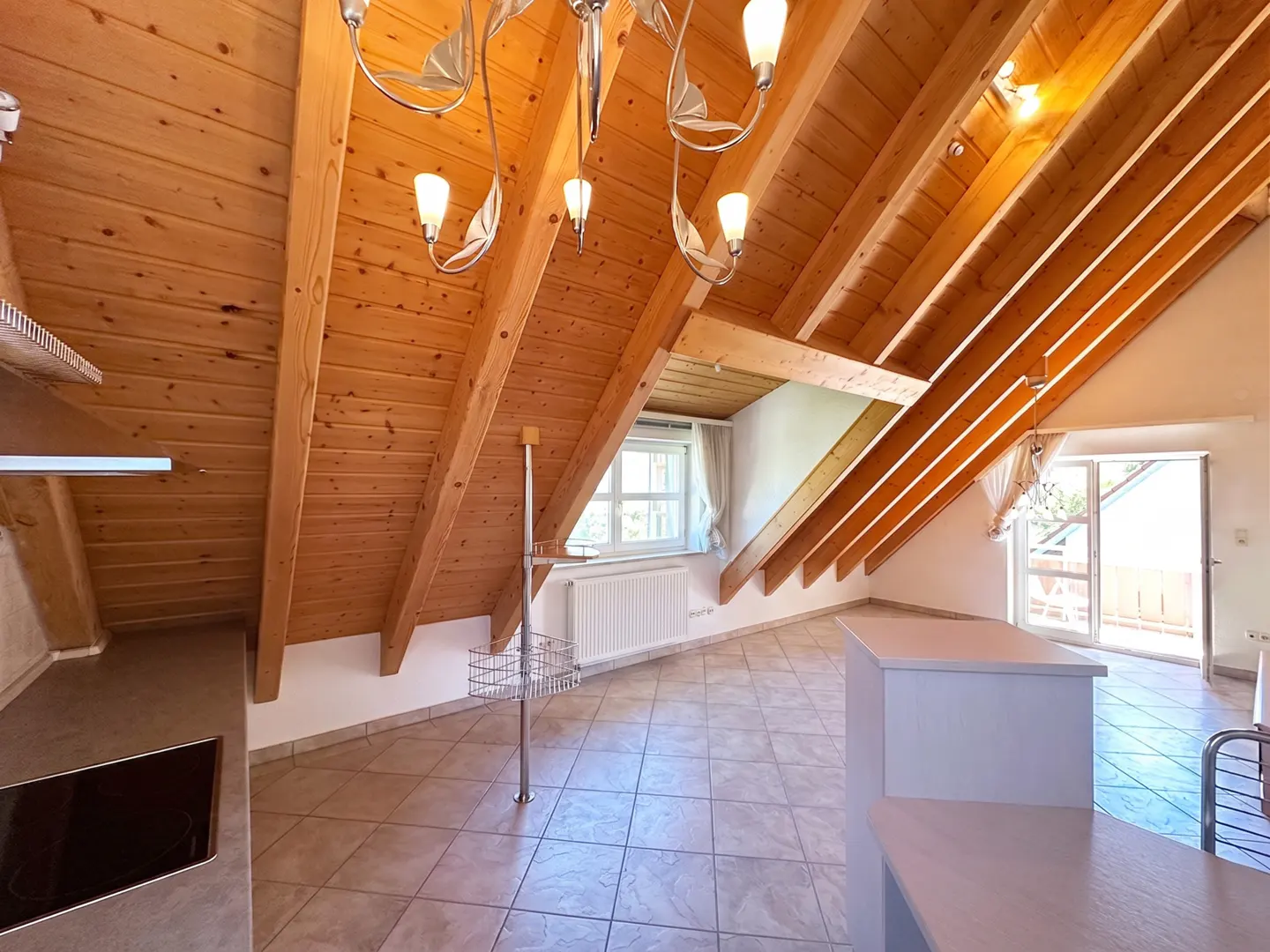 Attic apartment with wood ceiling, tile floor, white kitchen island, window, and balcony door.