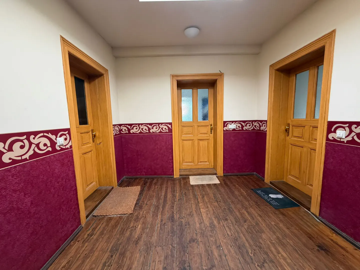 Hallway with three wooden doors, dark wood floors, and red walls with white patterned trim.