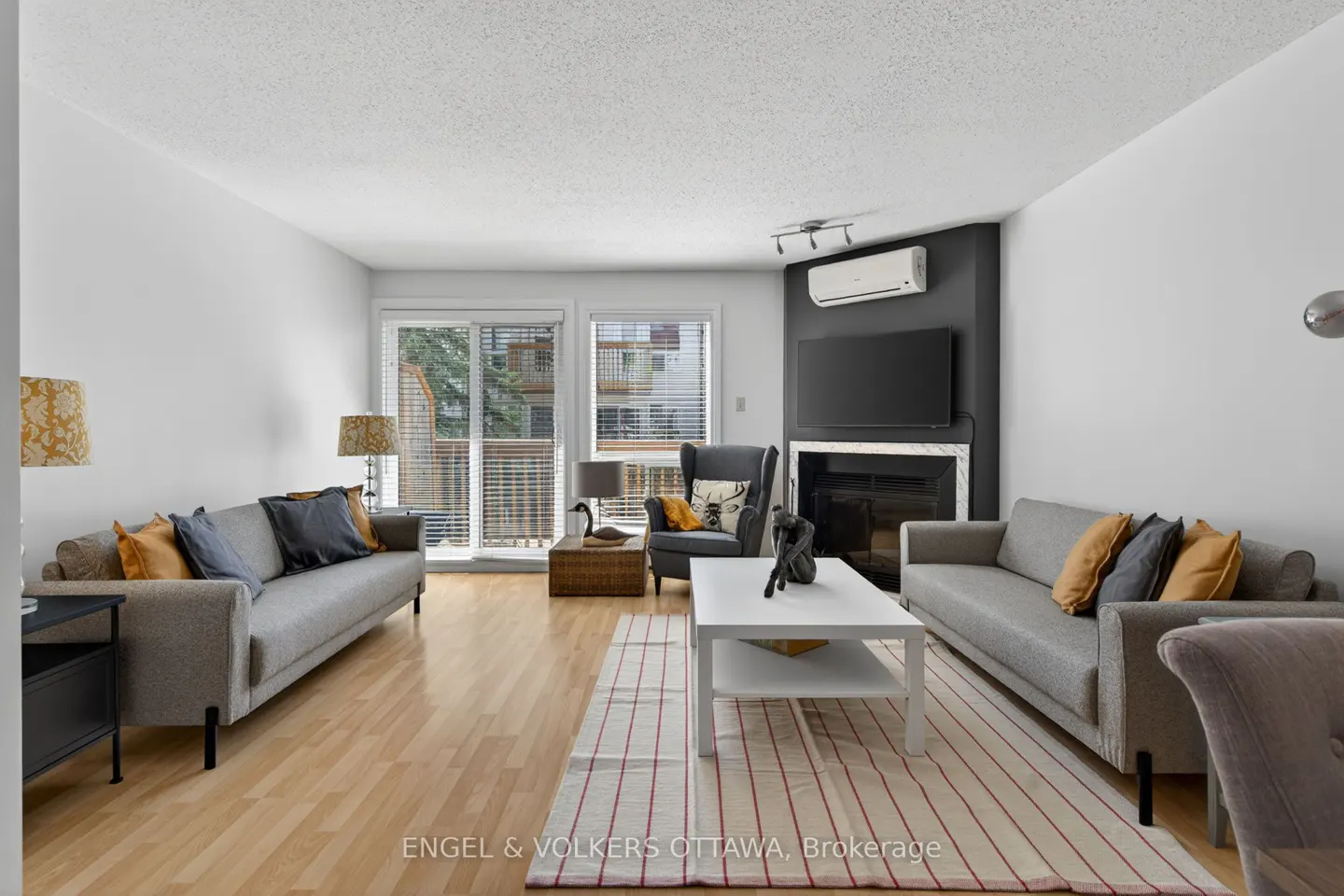 Bright living room with gray sofas, white coffee table, and fireplace. Sliding glass doors lead to a balcony. Hardwood floors and neutral decor.