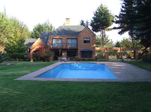 A two-story brick house with a pool and green lawn.