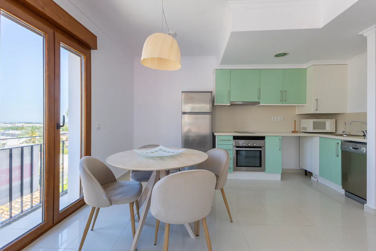 Bright kitchen with mint green cabinets, stainless steel appliances, and a round dining table with four chairs near a balcony door.