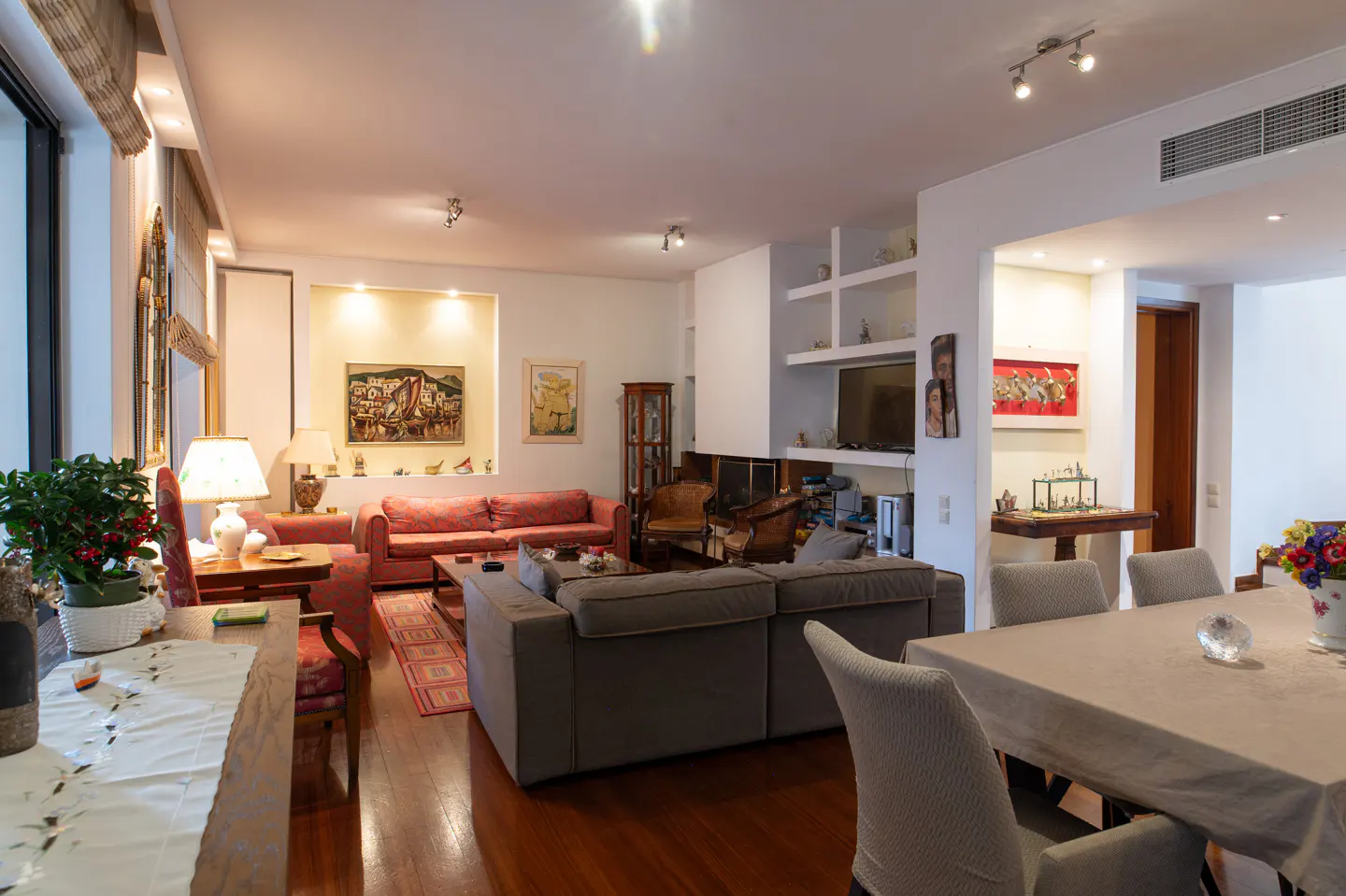A spacious living room with hardwood floors, sofas, art, and a dining table with chairs.