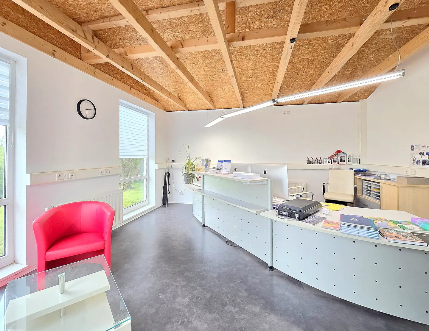 Bright office space with a red chair, white walls, and a wood-paneled ceiling. A large white desk sits in the center.