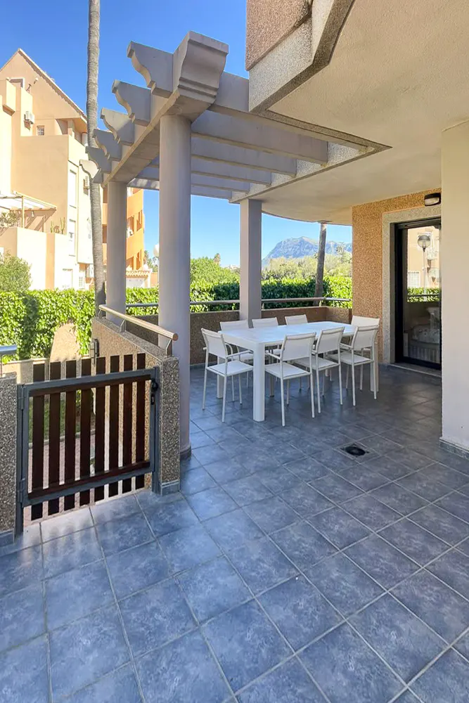 Outdoor patio with a white table and chairs under a pergola, overlooking green trees and a distant mountain.