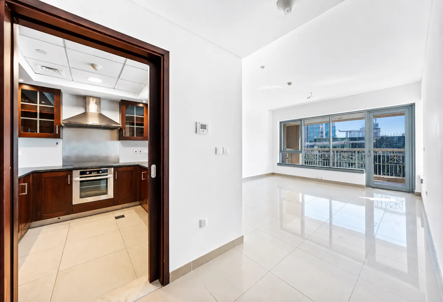 View of a modern kitchen with dark wood cabinets and stainless steel appliances, opening into a bright, tiled living area.