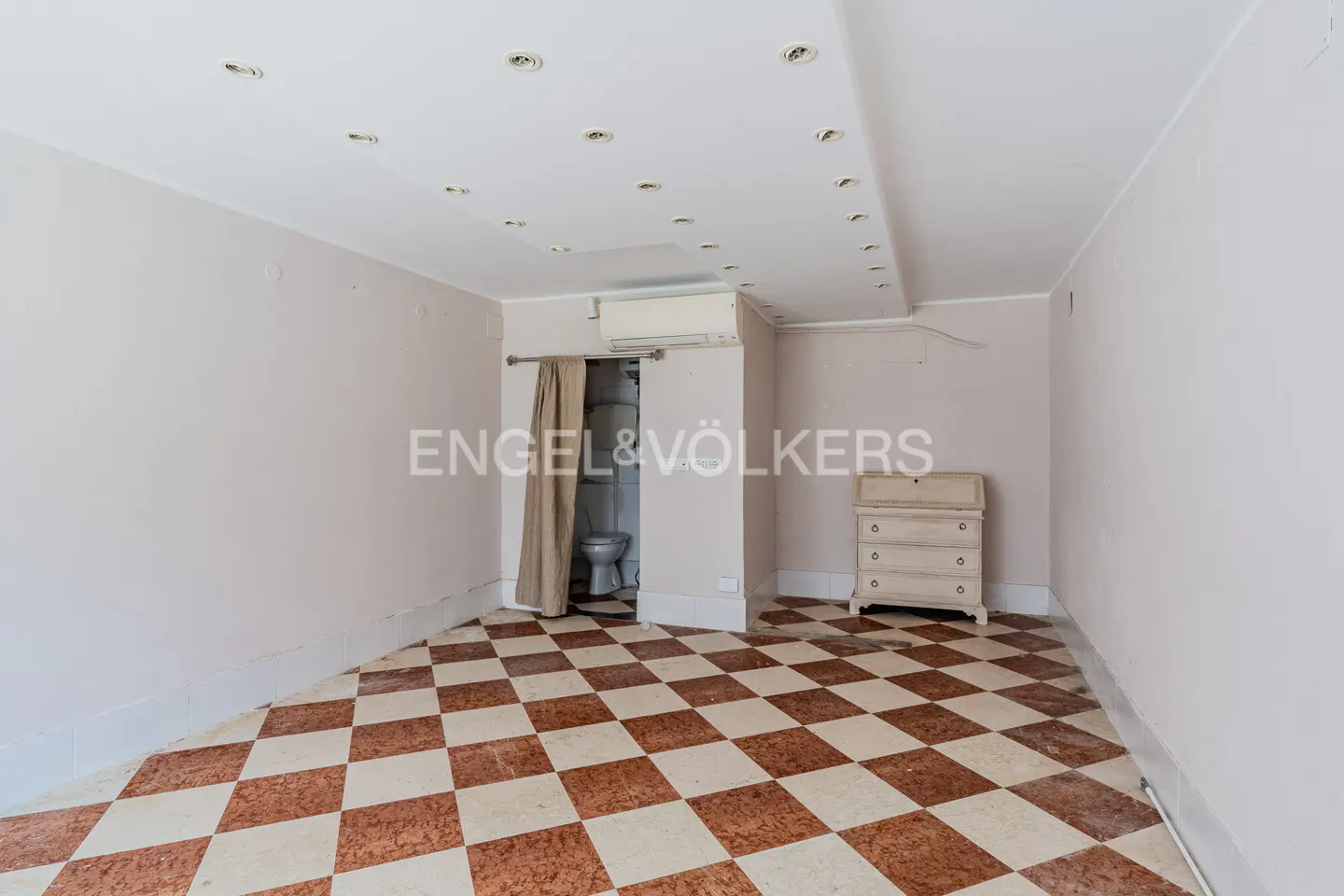A room with a checkered floor, white walls, and a toilet behind a curtain. A white dresser is on the right.